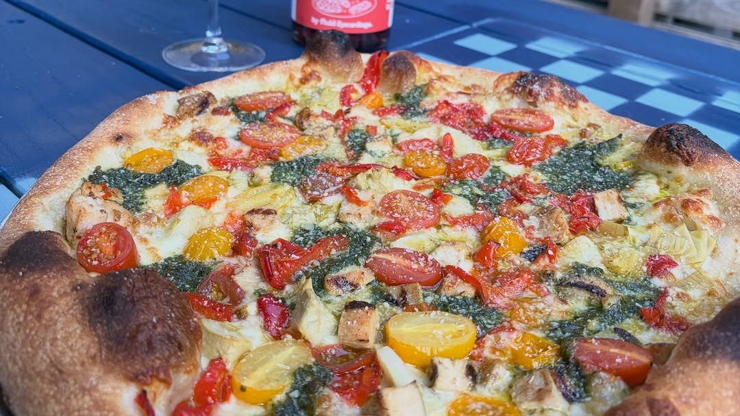 A Problem Child pizza and a glass of chilled red wine on a blue gingham table